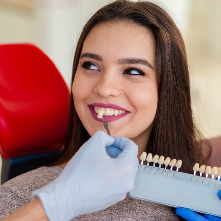 Woman's smile compared to porcelain veneer shade chart during cosmetic dentistry visit