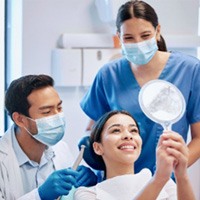 Dentist, dental assistant, and patient smiling at reflection in mirror