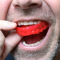 man putting a red mouthguard into his mouth