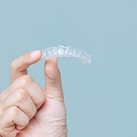 Patient holding Invisalign aligner against blue background