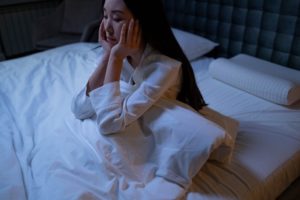 Woman sitting up in bed with her hands on her face